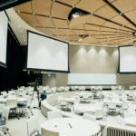 Modern corporate event setup with large projection screens, round tables, and professional lighting