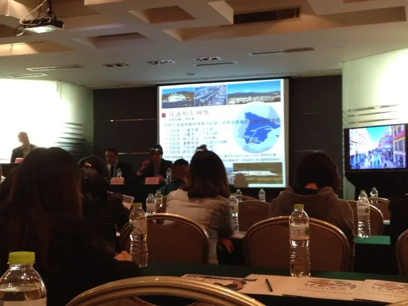 Setup for a MICE event in Malaga with a podium, professional lighting, sound equipment, a large screen displaying a presentation, and a projector in a modern conference venue.