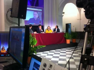 Setup for a MICE event in Malaga with a podium, professional lighting, sound equipment, a large screen displaying a presentation, and a projector in a modern conference venue.