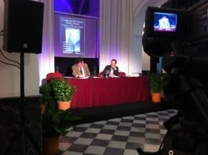 Setup for a MICE event in Malaga with a podium, professional lighting, sound equipment, a large screen displaying a presentation, and a projector in a modern conference venue.