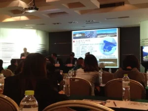 Setup for a MICE event in Malaga with a podium, professional lighting, sound equipment, a large screen displaying a presentation, and a projector in a modern conference venue.