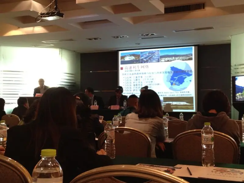 Setup for a MICE event in Malaga with a podium, professional lighting, sound equipment, a large screen displaying a presentation, and a projector in a modern conference venue.