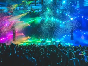A vibrant concert scene with colorful lights and confetti above a large crowd of excited attendees.