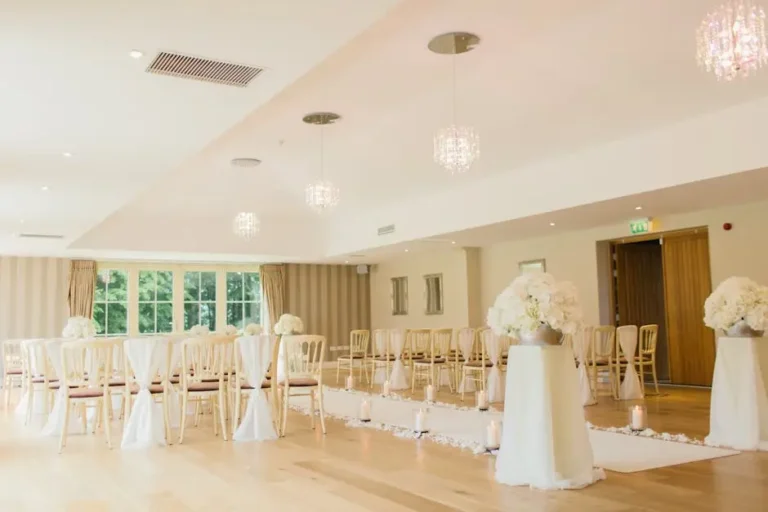 Elegant indoor wedding ceremony hall with white floral arrangements and chandeliers.
