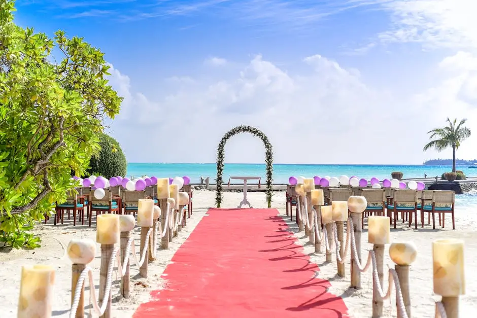 A beautiful beach wedding ceremony setup with a red carpet aisle and floral arch.
